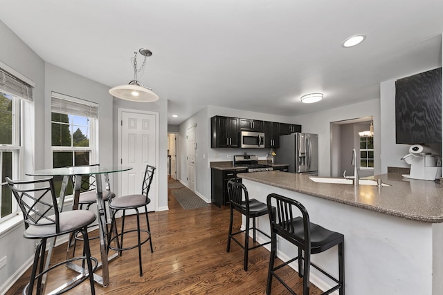 kitchen featuring sink, dark wood-type flooring, appliances with stainless steel finishes, a kitchen bar, and kitchen peninsula