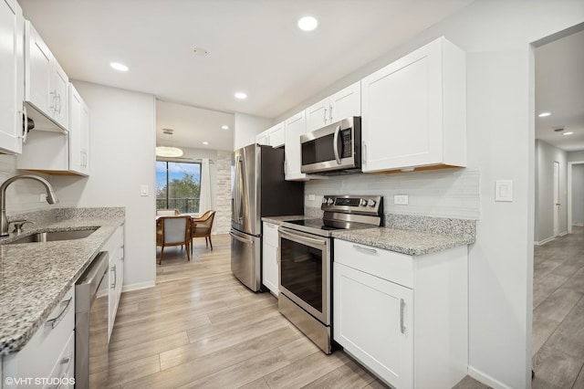 kitchen with sink, white cabinetry, light stone counters, stainless steel appliances, and light hardwood / wood-style floors