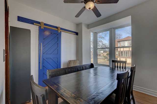 dining space featuring a barn door, hardwood / wood-style floors, and ceiling fan