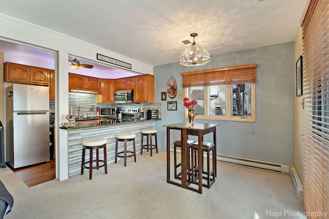 kitchen with sink, appliances with stainless steel finishes, a baseboard heating unit, decorative backsplash, and kitchen peninsula