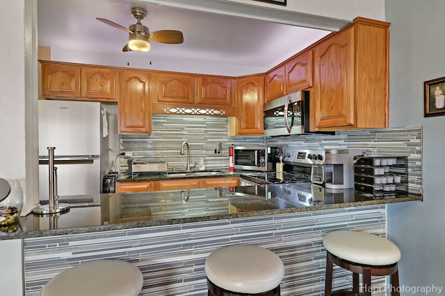 kitchen featuring sink, ceiling fan, backsplash, stainless steel appliances, and dark stone counters