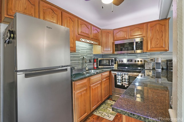 kitchen with dark stone countertops, stainless steel appliances, sink, and backsplash