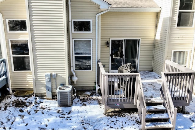 snow covered property entrance featuring a wooden deck and central air condition unit