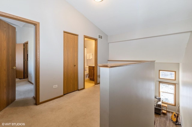 hall featuring lofted ceiling and light colored carpet