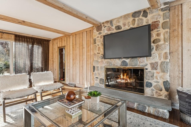 living room featuring beam ceiling, a stone fireplace, and hardwood / wood-style flooring