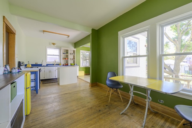 dining room with sink, light hardwood / wood-style flooring, and beamed ceiling