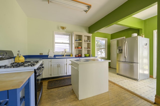 kitchen with a kitchen island, sink, white cabinets, stainless steel fridge, and gas stove