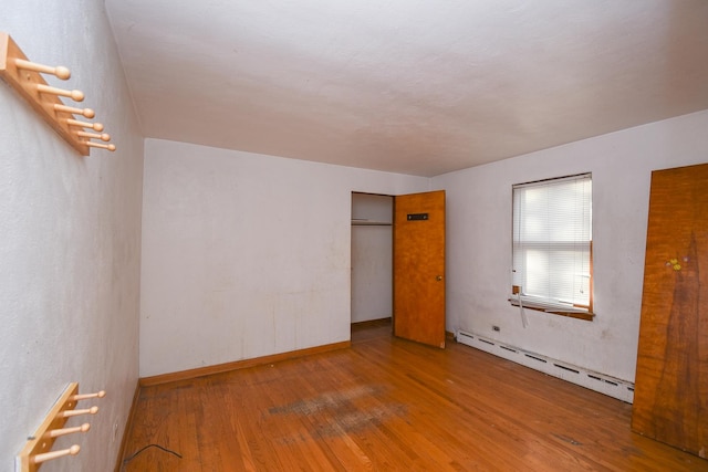 unfurnished bedroom with a baseboard heating unit and wood-type flooring