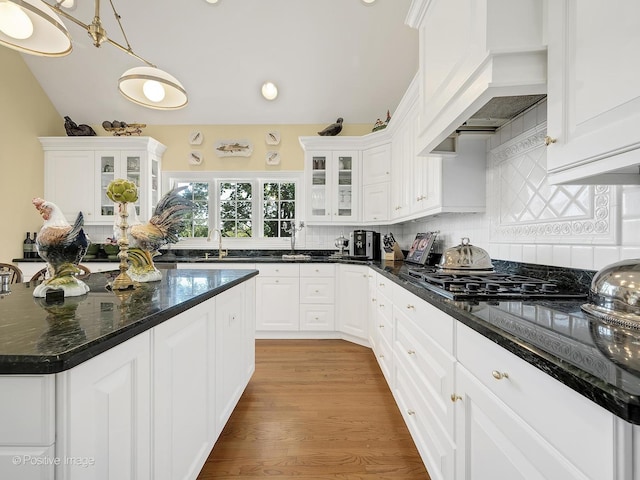 kitchen featuring hanging light fixtures, custom range hood, dark stone countertops, and white cabinets