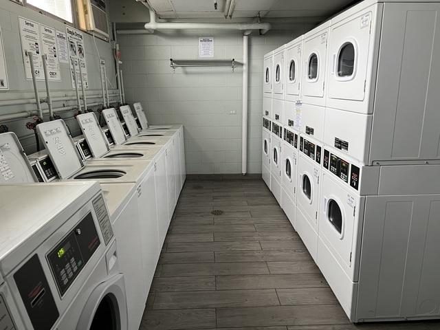 common laundry area featuring washer and dryer, stacked washer and dryer, concrete block wall, and dark wood-style flooring