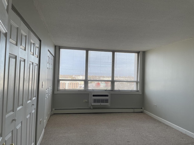 carpeted spare room featuring baseboard heating, a textured ceiling, a wall mounted air conditioner, and baseboards