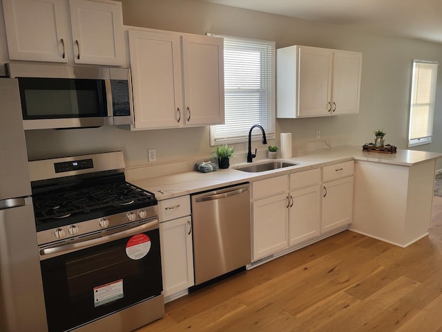 kitchen featuring stainless steel appliances, kitchen peninsula, sink, and white cabinets