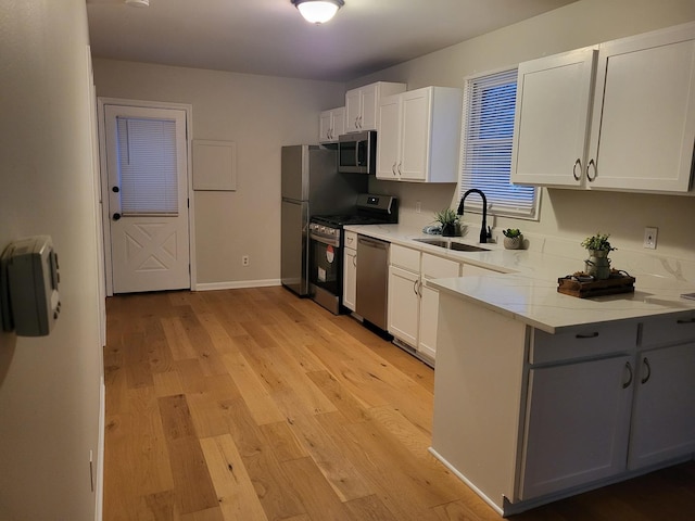 kitchen with sink, stainless steel appliances, light hardwood / wood-style floors, light stone countertops, and white cabinets