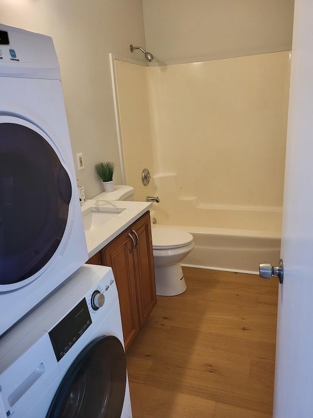 full bathroom with stacked washing maching and dryer, shower / washtub combination, hardwood / wood-style flooring, vanity, and toilet