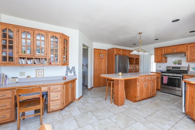 kitchen with a center island, built in desk, a kitchen breakfast bar, pendant lighting, and stainless steel appliances