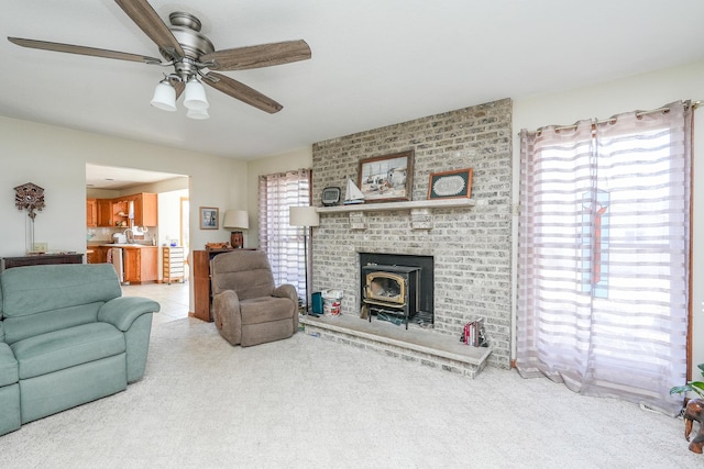 carpeted living room with a wood stove and ceiling fan