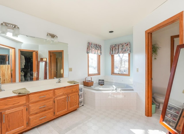 bathroom featuring vanity, tiled tub, and toilet