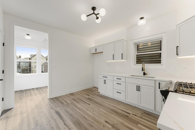 kitchen featuring sink, white cabinetry, light stone counters, range, and light hardwood / wood-style floors