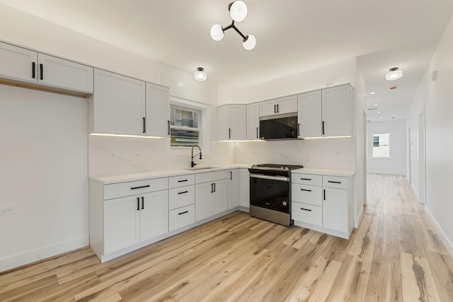 kitchen with tasteful backsplash, stainless steel range oven, sink, and light hardwood / wood-style flooring