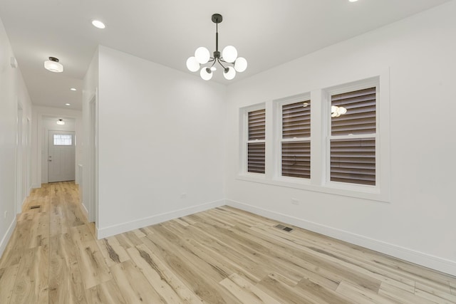 spare room with a chandelier and light wood-type flooring