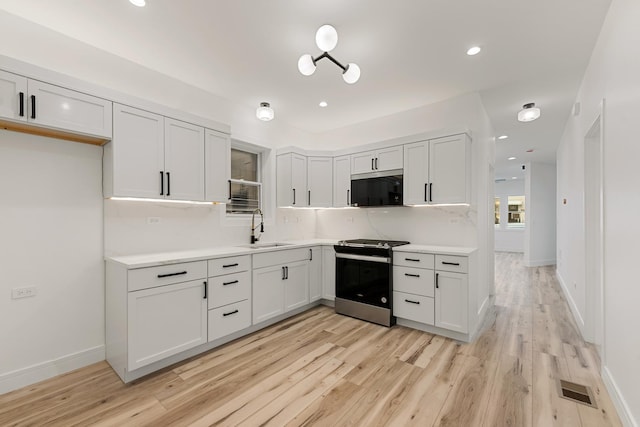 kitchen with appliances with stainless steel finishes, white cabinetry, sink, backsplash, and light hardwood / wood-style floors