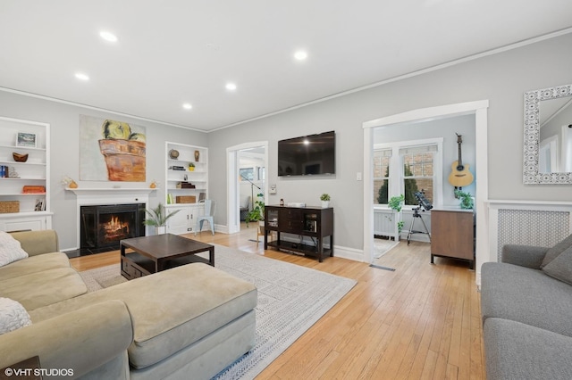 living room featuring ornamental molding, built in features, and light wood-type flooring