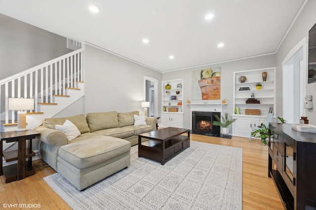 living room featuring crown molding, built in features, and light wood-type flooring