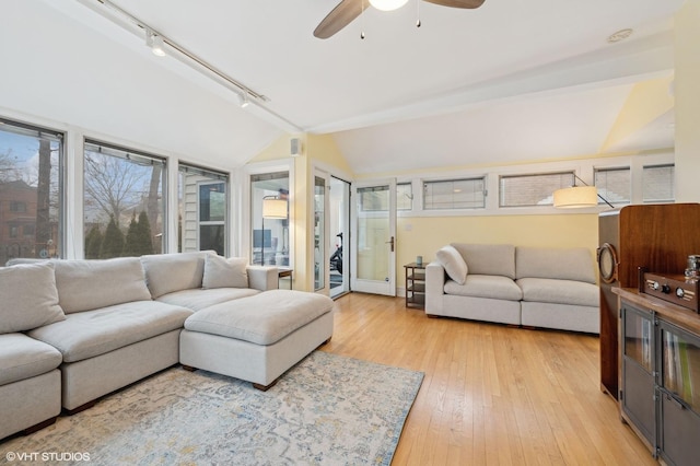 living room featuring vaulted ceiling, light hardwood / wood-style floors, rail lighting, and ceiling fan