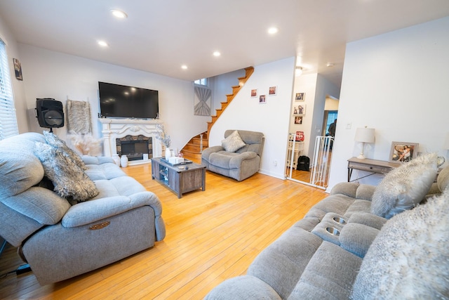 living room with wood-type flooring, stairs, a fireplace with raised hearth, and recessed lighting