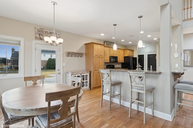 kitchen featuring light brown cabinetry, kitchen peninsula, light stone countertops, light hardwood / wood-style floors, and black appliances