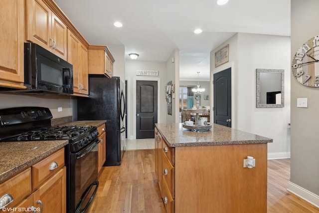 kitchen featuring dark stone countertops, a center island, a notable chandelier, light hardwood / wood-style floors, and black appliances