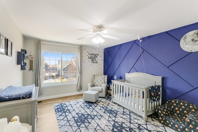 bedroom featuring a crib, ceiling fan, and light hardwood / wood-style floors