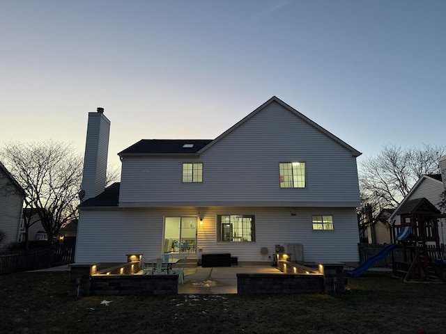 back house at dusk featuring a fire pit, a patio area, and a playground