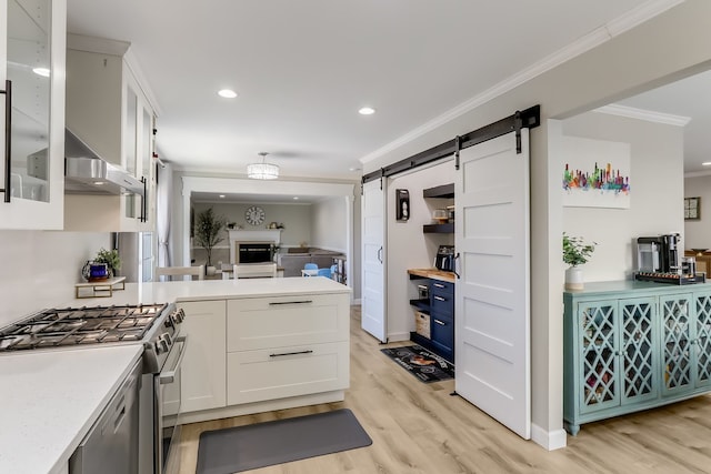 kitchen featuring white cabinetry, ornamental molding, stainless steel appliances, a barn door, and wall chimney range hood