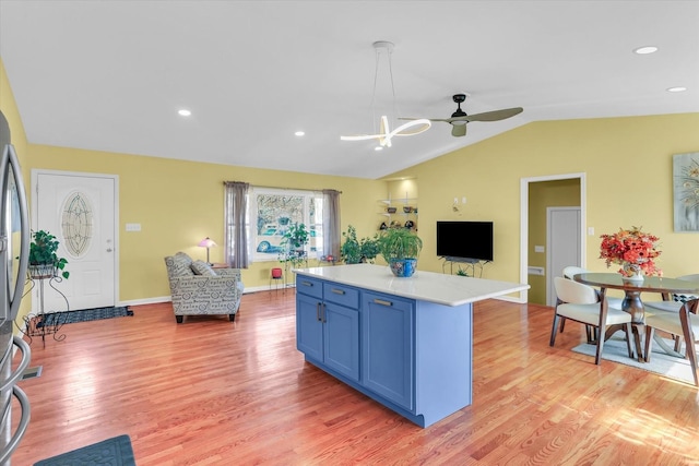 kitchen with blue cabinetry, hanging light fixtures, a center island, vaulted ceiling, and light wood-type flooring