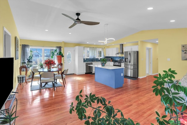 kitchen featuring wall chimney exhaust hood, white cabinetry, a center island, pendant lighting, and stainless steel appliances