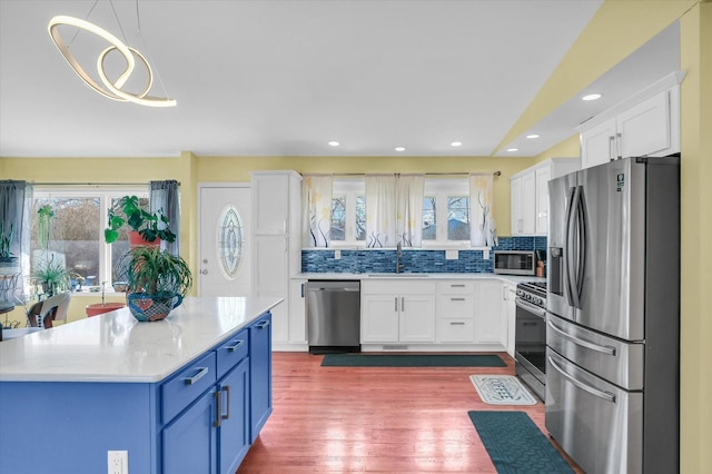 kitchen with blue cabinetry, sink, pendant lighting, stainless steel appliances, and white cabinets