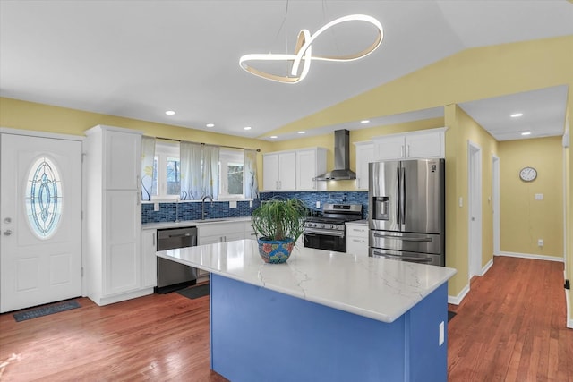 kitchen with white cabinetry, a center island, hanging light fixtures, appliances with stainless steel finishes, and wall chimney range hood