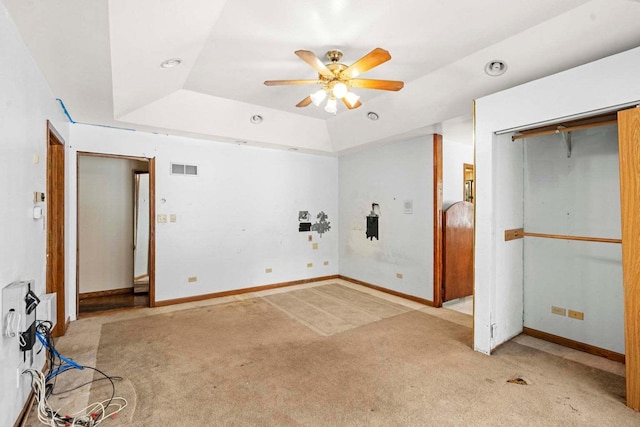 unfurnished bedroom with a closet, light colored carpet, ceiling fan, and a tray ceiling