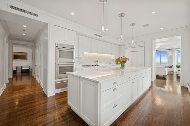 kitchen featuring pendant lighting, appliances with stainless steel finishes, a center island, tasteful backsplash, and white cabinets