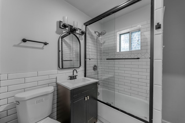 full bathroom with vanity, toilet, combined bath / shower with glass door, and tile walls