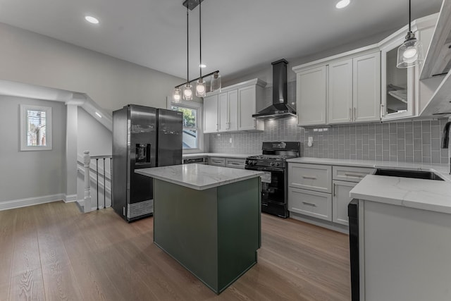 kitchen with black gas range oven, wall chimney range hood, refrigerator with ice dispenser, a center island, and white cabinets