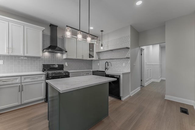 kitchen with pendant lighting, wall chimney range hood, a center island, black appliances, and light stone countertops