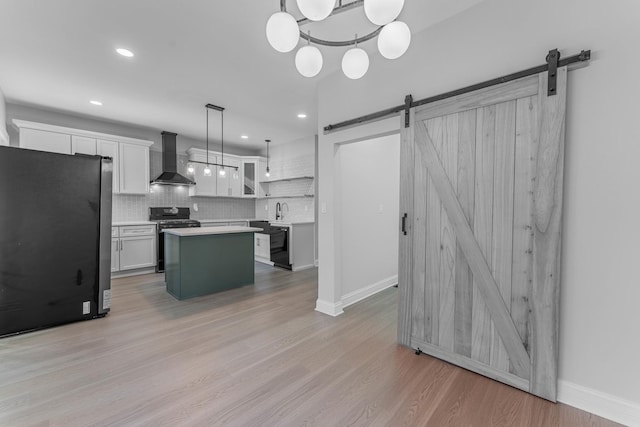 kitchen with gas stove, hanging light fixtures, a kitchen island, a barn door, and wall chimney range hood