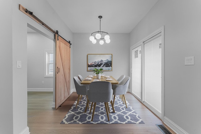 dining area with a notable chandelier, wood-type flooring, and a barn door