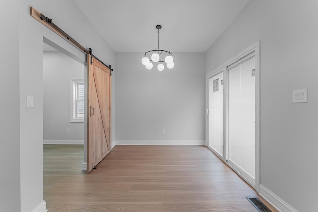 unfurnished dining area with an inviting chandelier, light hardwood / wood-style flooring, and a barn door