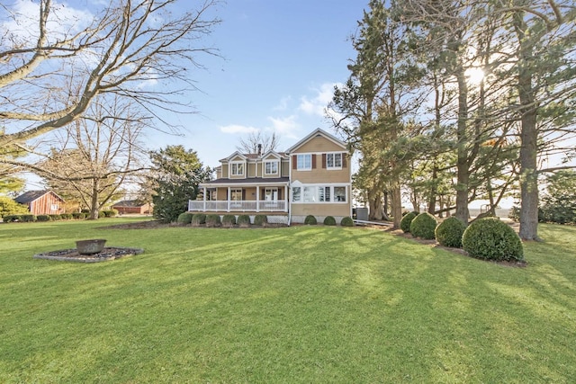 rear view of house with a porch, a fire pit, and a lawn