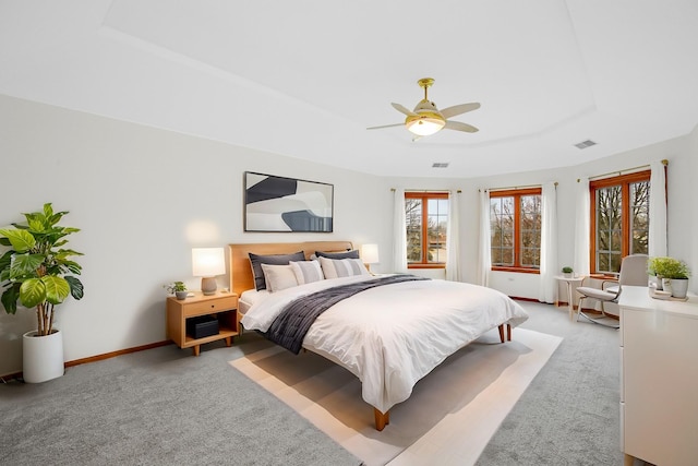 bedroom with a tray ceiling, light carpet, and multiple windows