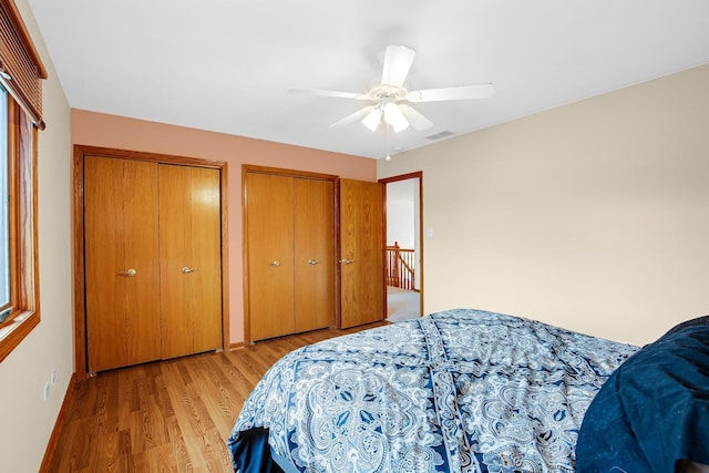 bedroom with ceiling fan, light hardwood / wood-style floors, and two closets