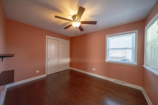 unfurnished bedroom with multiple windows, dark wood-type flooring, a closet, and ceiling fan